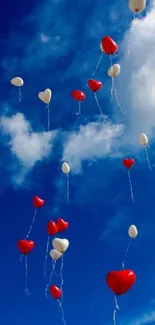 Red and white heart-shaped balloons floating in a bright blue sky with clouds.