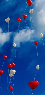 Red and white heart balloons float in blue sky with clouds.