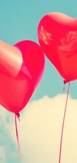 Red heart balloons floating in a blue sky.