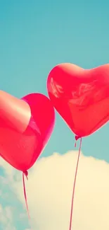 Two red heart-shaped balloons float in a bright blue sky.