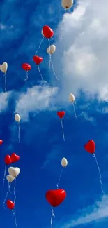 Red and white heart balloons floating in a bright blue sky with clouds.