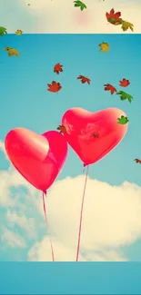 Two heart-shaped balloons floating in a clear blue sky with colorful leaves.