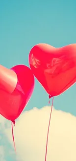 Red heart balloons float against a blue sky with clouds.