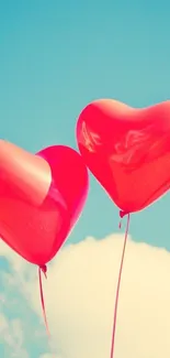 Two red heart-shaped balloons float against a clear blue sky with clouds.