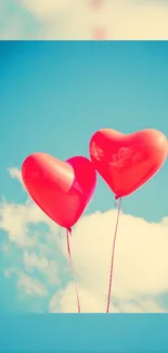 Two heart-shaped red balloons float against a bright blue sky with clouds.