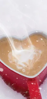 Heart-shaped red mug of coffee in snow with steam rising.