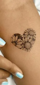 Heart-shaped floral tattoo on skin with sunflowers.