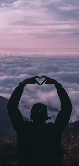 Silhouette of a heart shape against pink clouds at sunset over mountains.