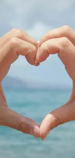 Hands forming a heart shape over a blue ocean background.