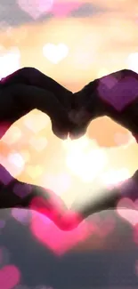 Hands forming heart shape against sunset with pink heart bokeh effect.