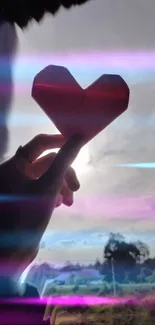 Hand holding origami heart with pink light streaks in a scenic setting.