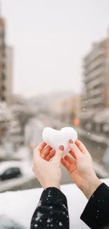 Person holding a snow heart in cityscape.