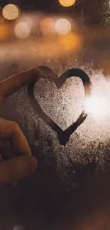 Heart drawn on a foggy window illuminated by warm city lights.