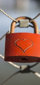 Red heart padlock hanging on a wire fence.