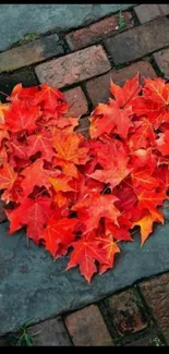 Heart made of red autumn leaves on a brick path background.