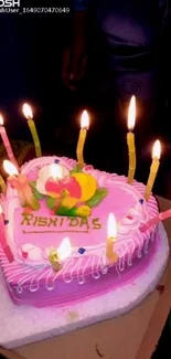 Heart-shaped cake with pink icing and lit candles on top.