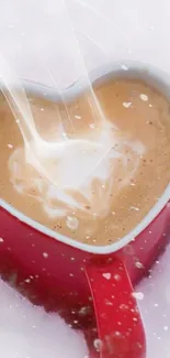 Heart-shaped red coffee mug with creamy latte art in snow.