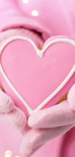 Heart-shaped pink cookie held in gloved hands, soft lighting.