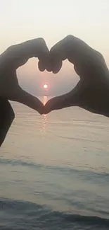 Heart-shaped hands framing ocean sunset.