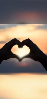 Silhouette of hands forming a heart at sunset with an orange glow.