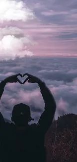 Silhouette making heart sign over pink cloud landscape.