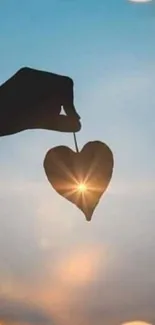 Silhouette of a hand holding a heart with sunset glow and bokeh sky.