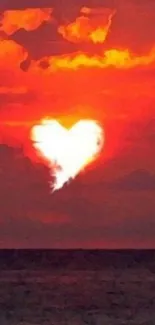 Heart-shaped cloud in sunset over ocean with vibrant orange hues.