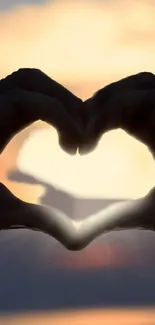Silhouette of heart-shaped hands against a vibrant sunset.