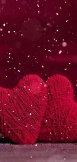 Two red yarn hearts in snowfall on maroon background.