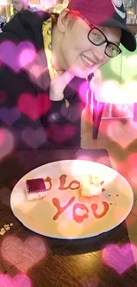 A person smiles in a cafe with a dessert plate that reads 'I love you' in syrup.