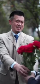 Man offers vibrant red flowers outdoors.