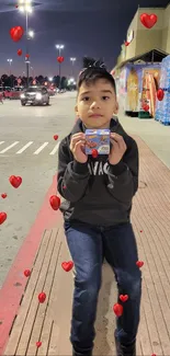 Boy holding card with heart graphics on a night street.