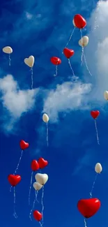 Red and white heart balloons float in vibrant blue sky.