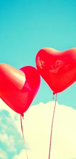 Two red heart balloons float against a sunny blue sky.