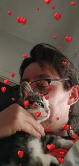 Person holding a kitten with red hearts in the air.