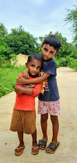 Two children hugging on a rural path with green surroundings.