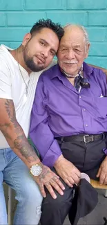 Father and son embracing against a teal wall.