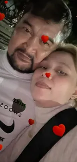 Cozy couple's selfie with red hearts overlay.