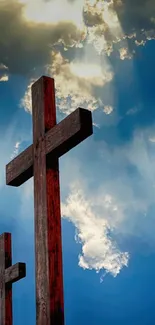 Two wooden crosses under a blue sky with clouds and light rays.