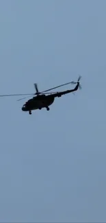 Silhouetted helicopter flying in a clear blue sky.