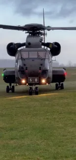 Military helicopter on a green field ready for takeoff under cloudy skies.