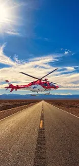 Red helicopter flying over a vast desert road beneath a vibrant blue sky.