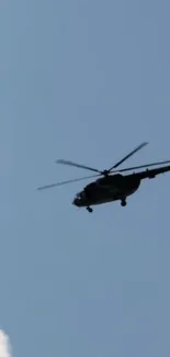 Silhouette of a helicopter flying in a blue sky.