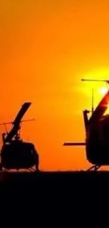 Silhouette of helicopters at sunset with vibrant orange sky.