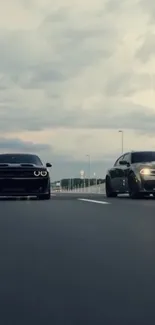 Two muscle cars on an open highway under a dramatic, cloudy sky.