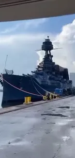 Battleship docked at port with cloudy sky backdrop.