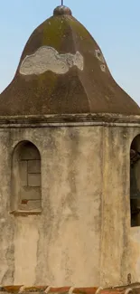 Rustic bell tower with stone facade and cross in serene setting.