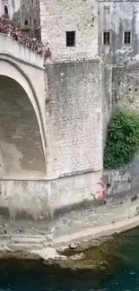 Diver leaps off historic stone bridge into river.