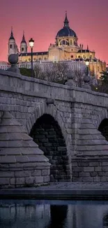 A historic stone bridge leading to a majestic cathedral at dusk under a pink-purple sky.