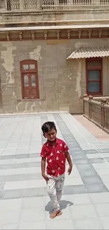 Young boy walking by a historic building facade on a sunny day.